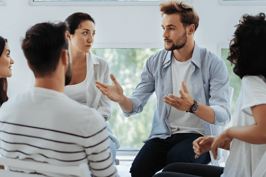 Group therapy session with diverse young adults listening.
