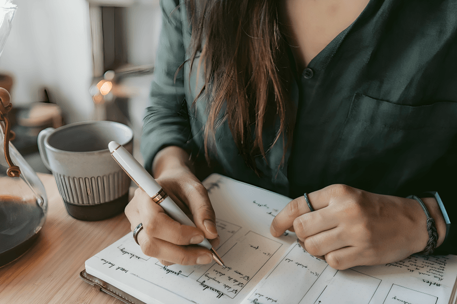 Person writing in a 'Gratitude Journal' on the desk.