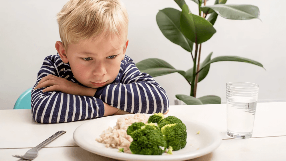 Blond boy frowning at a plate of broccoli and rice.