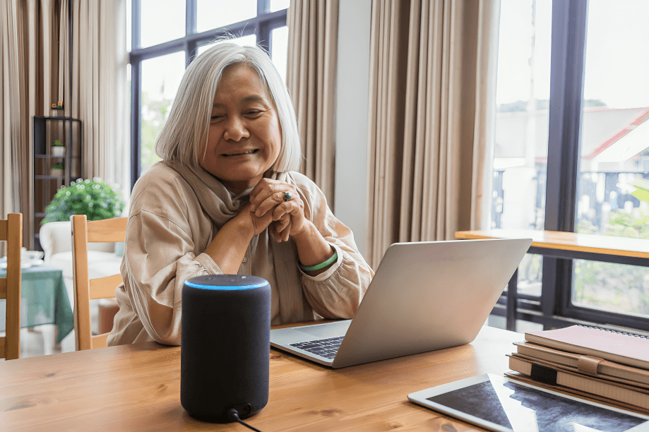 Smiling senior woman with laptop and smart speaker.