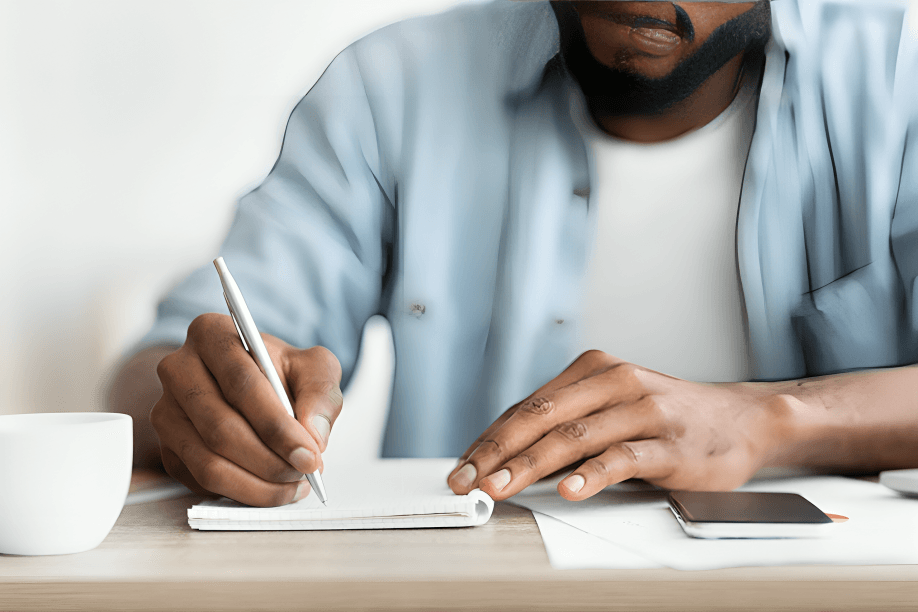 A man, possibly of African descent, writing in a notebook.