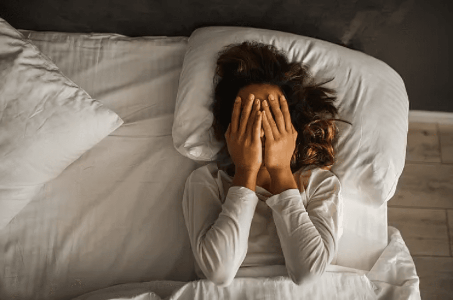 Woman in bed with hands covering her face.
