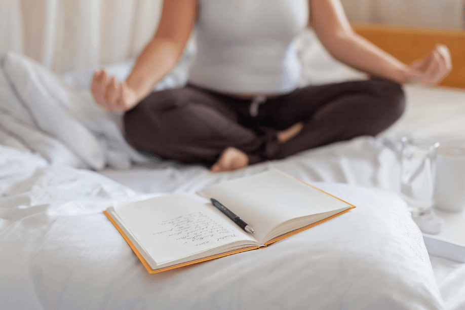 Person meditating with journal and pen on bed.