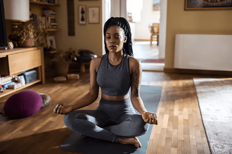 Woman with braids meditating in a sunlit room.