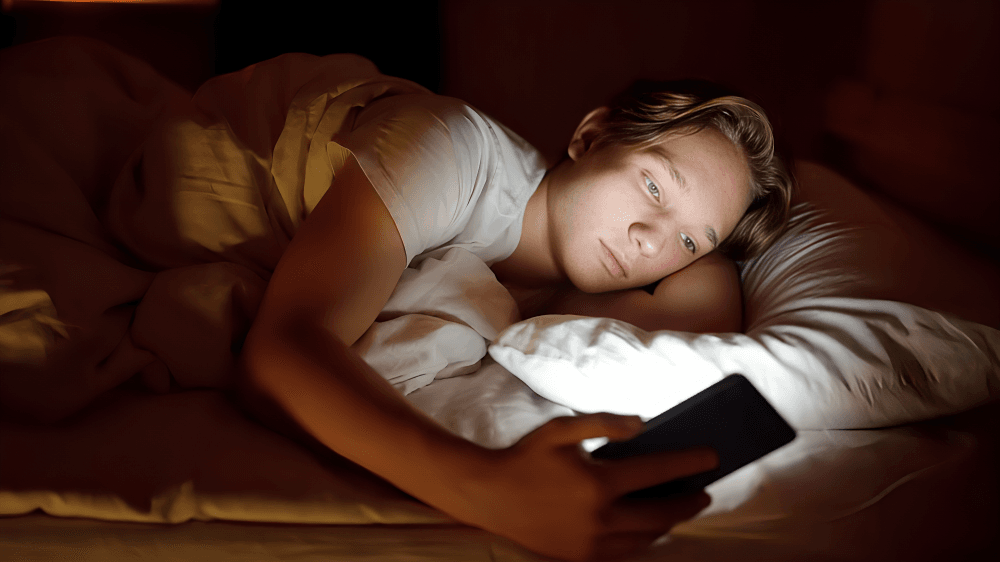 A person in bed looks at a glowing phone.