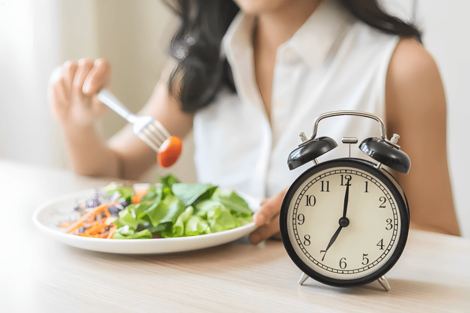 A woman eating salad, alarm clock nearby.