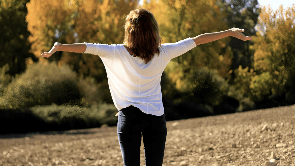 A woman with open arms standing in a green environment.