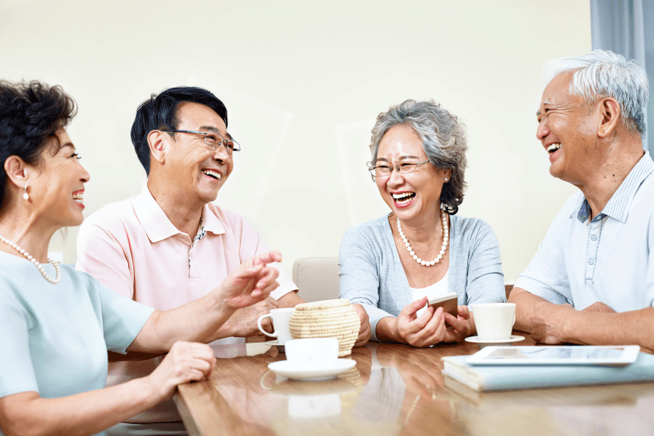 Four older adults, likely East Asian, laugh together at a table.
