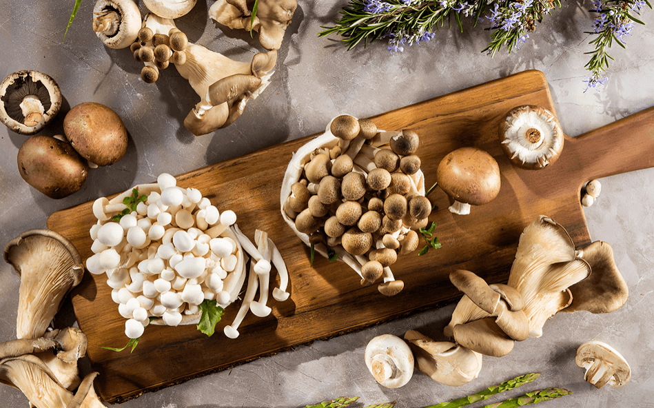 A variety of fresh mushrooms on a wooden cutting board.