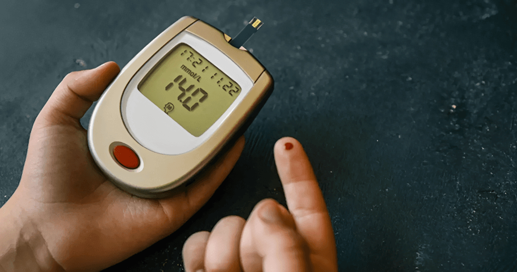 Hand holding glucose meter showing 14.0, blood drop on finger.