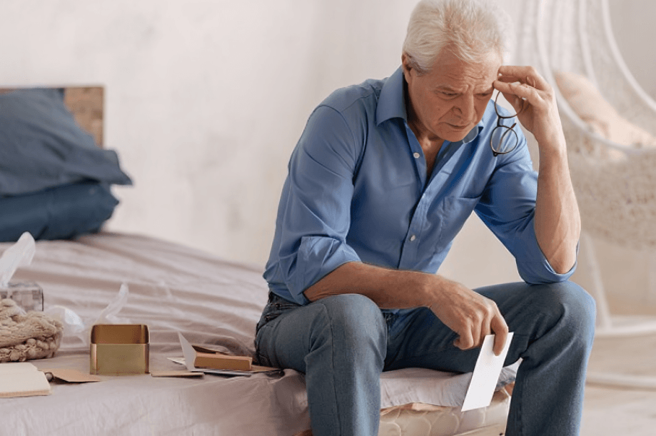 An elderly man looks sadly at a paper.