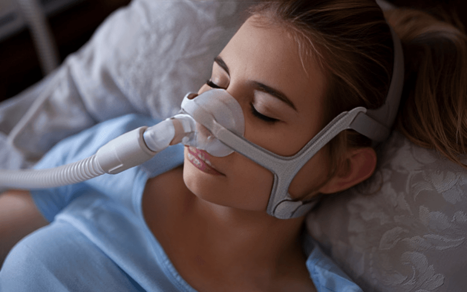 Person sleeping with CPAP machine on bedside table.