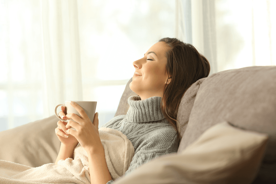 Woman relaxing on couch with warm drink, eyes closed.
