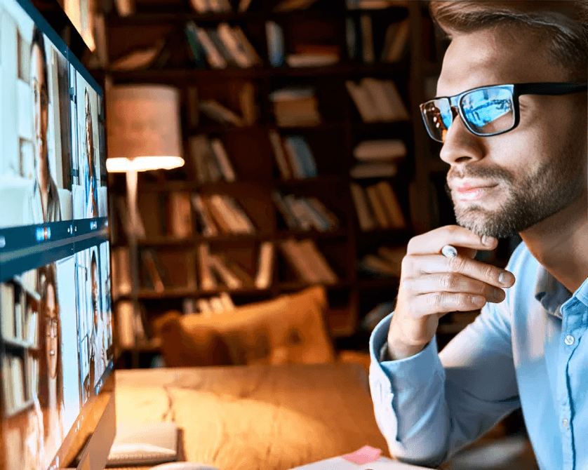Man with glasses in video call, bookshelf background.