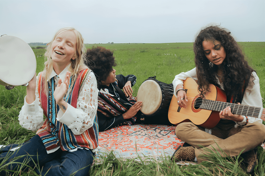 Three people play music outdoors on a blanket.
