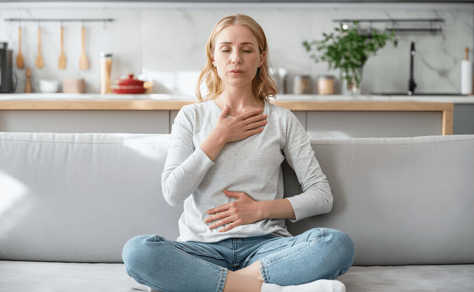 Blonde woman meditating on couch with hands on torso.
