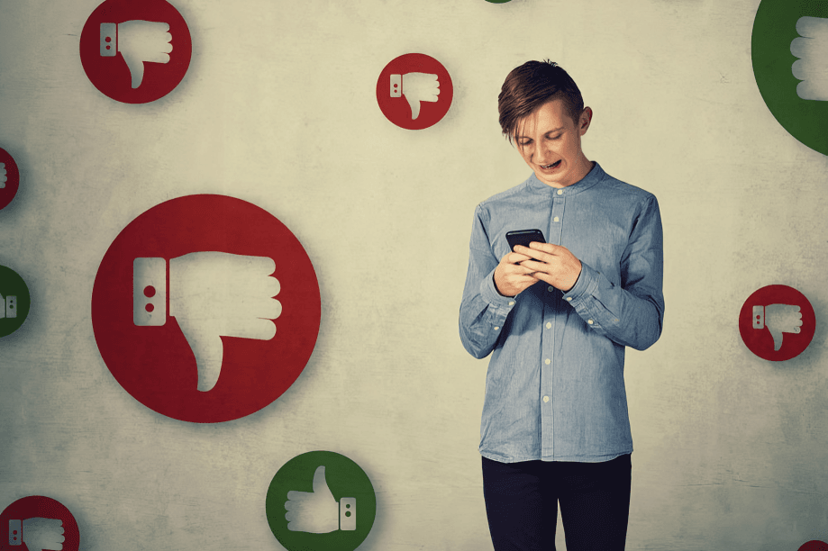 A young male looks at a phone surrounded by thumbs down.