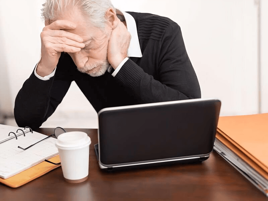 Man holding head, looking stressed at his laptop.