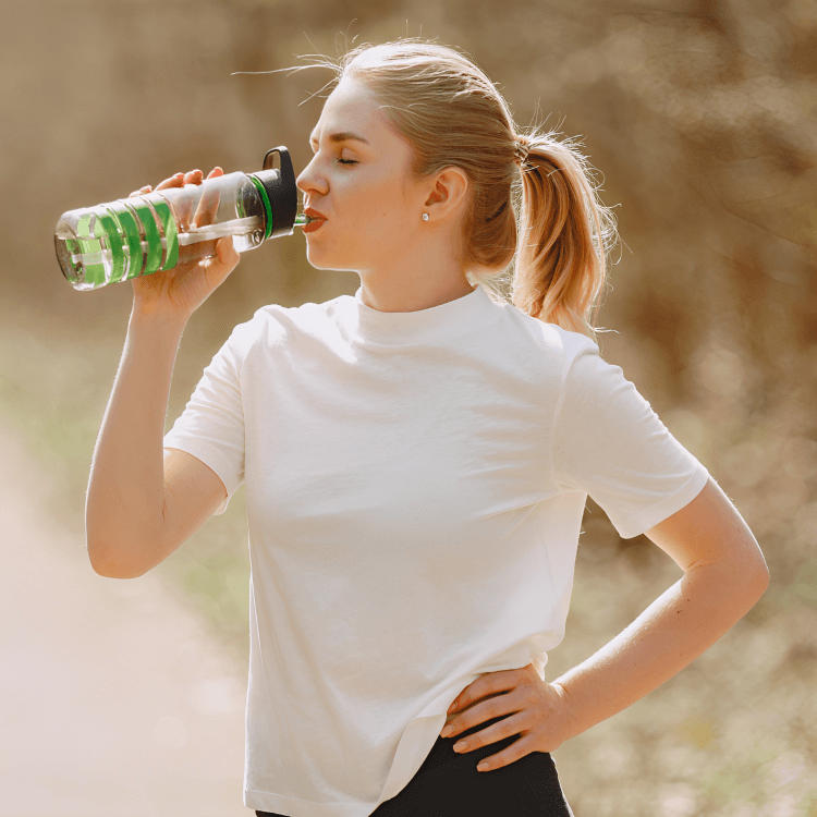 Young woman in a white shirt drinking water outdoors.