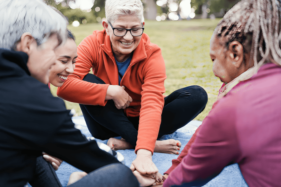 Diverse older women stack hands, smiling outdoors.
