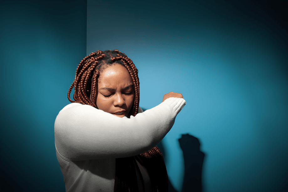 Woman in white top sneezing into her elbow.