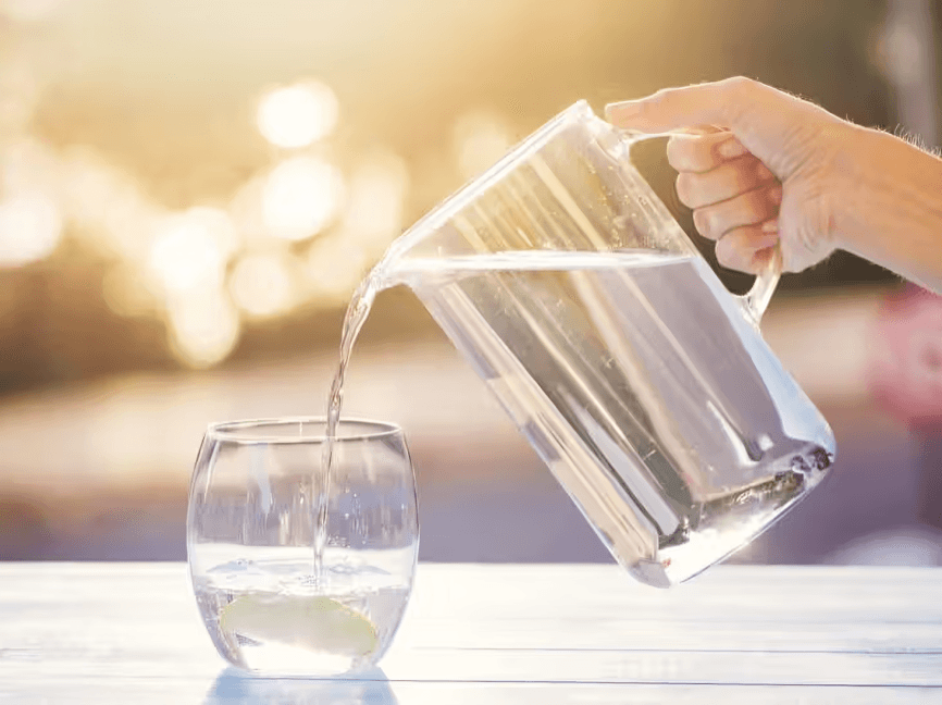 Hand pouring water from a pitcher into a glass.