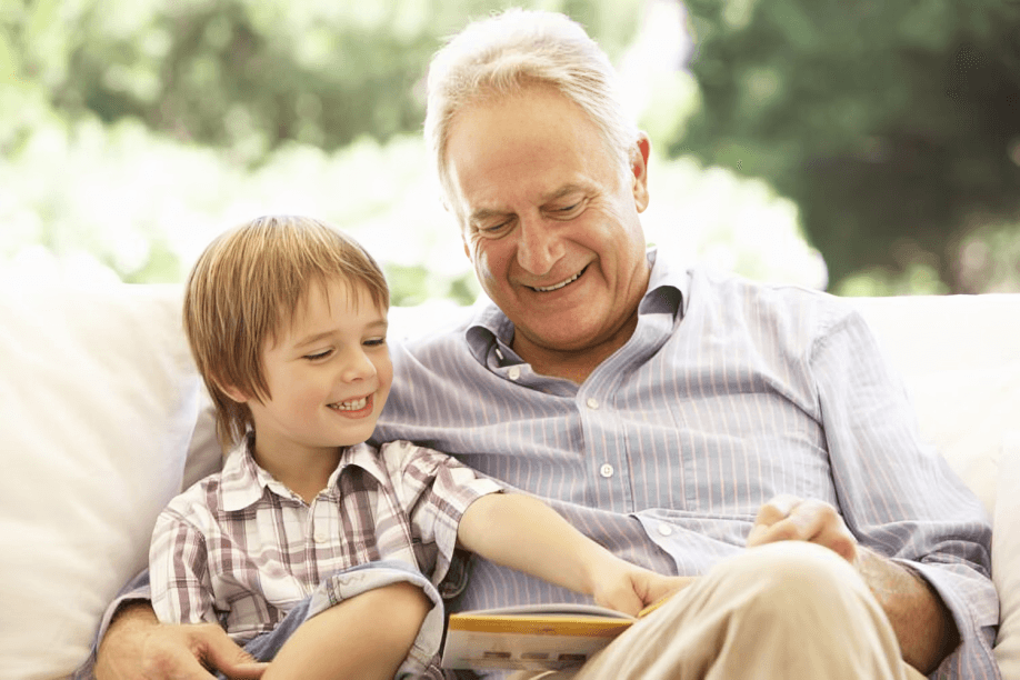 Grandfather and grandson smiling while reading a book.