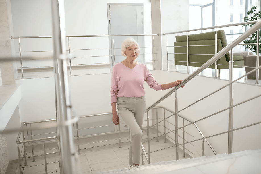 Older woman with white hair walking down a staircase indoors.