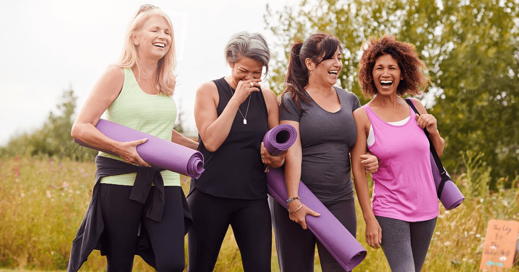 A group of women with yoga mats walking and smiling on the grass.