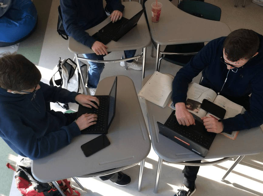 Students at desks using laptops, seen from above.