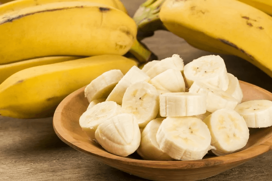 Sliced bananas in a bowl with whole bananas nearby.