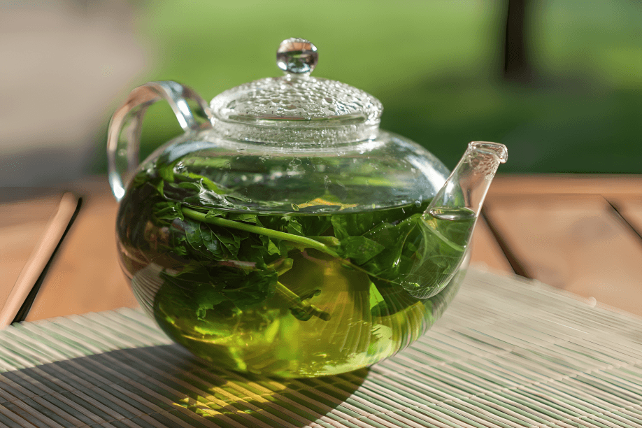 Glass teapot steeping fresh peppermint tea on table.