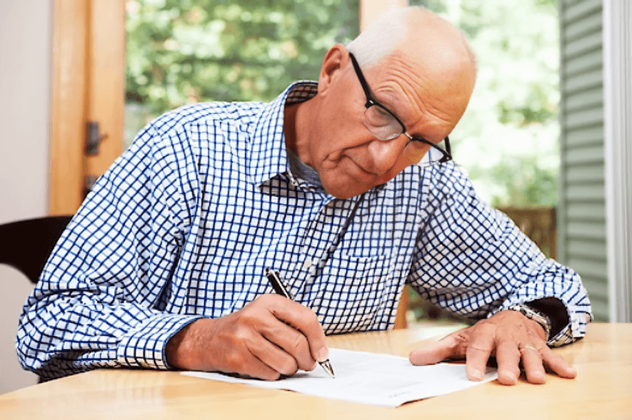 A man wearing glasses signing a document at a table.