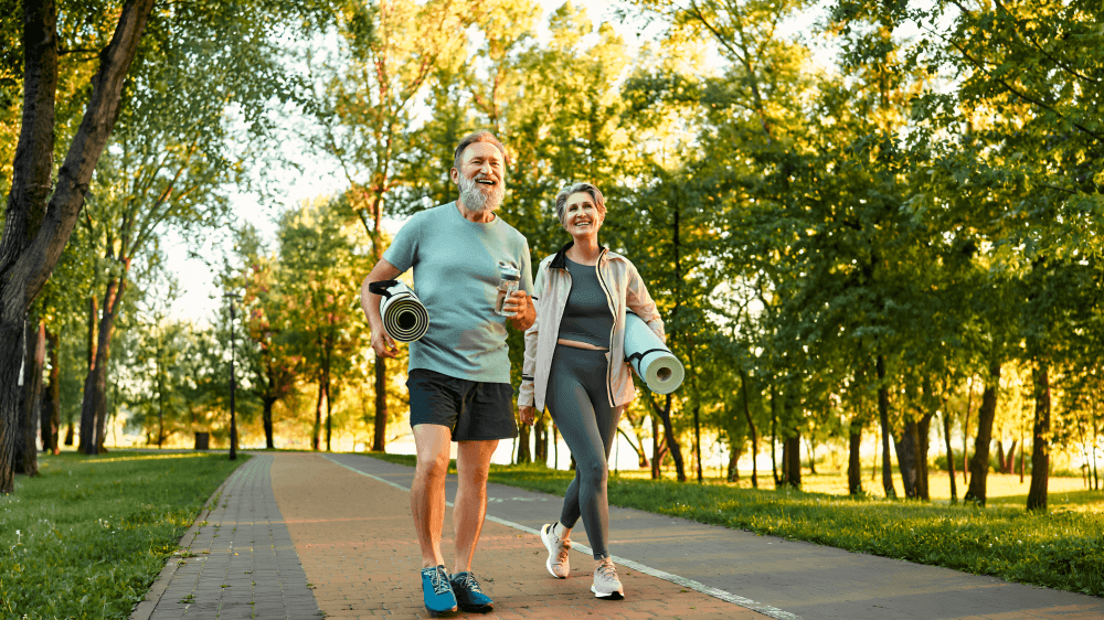Happy seniors walking with yoga mats in the park.
