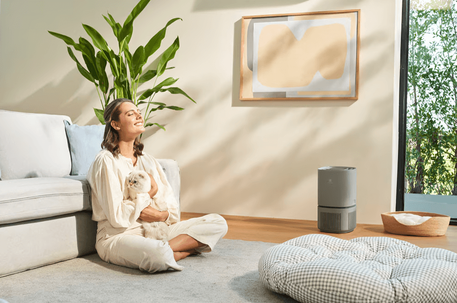 Woman sitting on floor, holding cat, near air purifier.