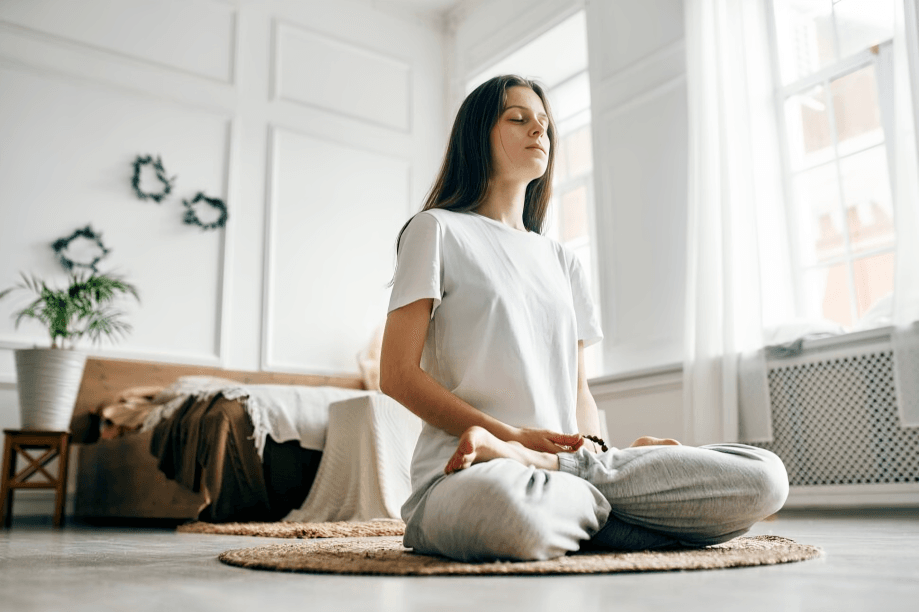 A young woman meditating in a lotus position at home.