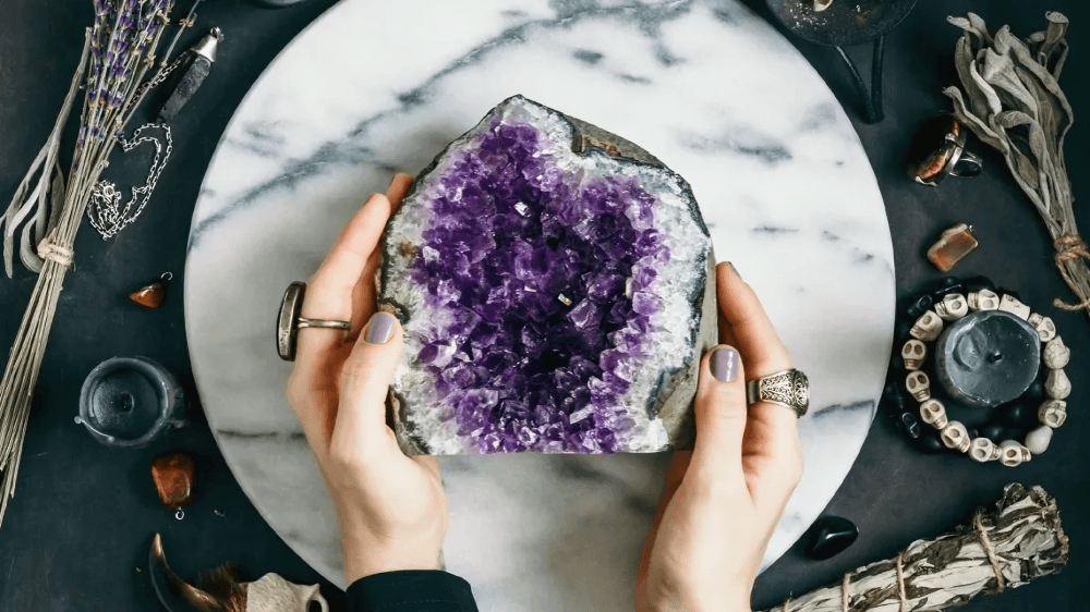 Hands holding a large amethyst geode on a marble board.