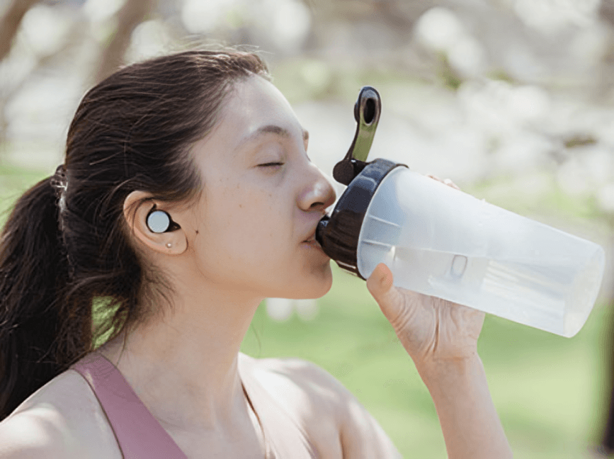 A woman with earbuds drinks from a water bottle.
