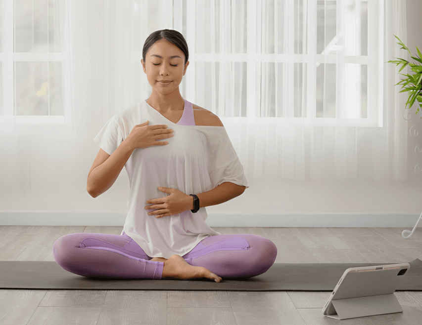 Woman meditating indoors with hands on chest and abdomen.