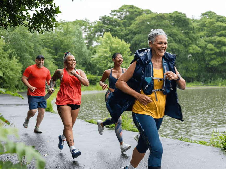 A diverse group of people jogging happily along a waterside path.
