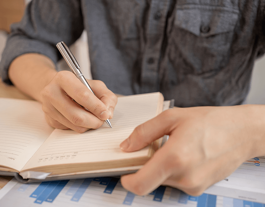 Person writing in a notebook with a pen.