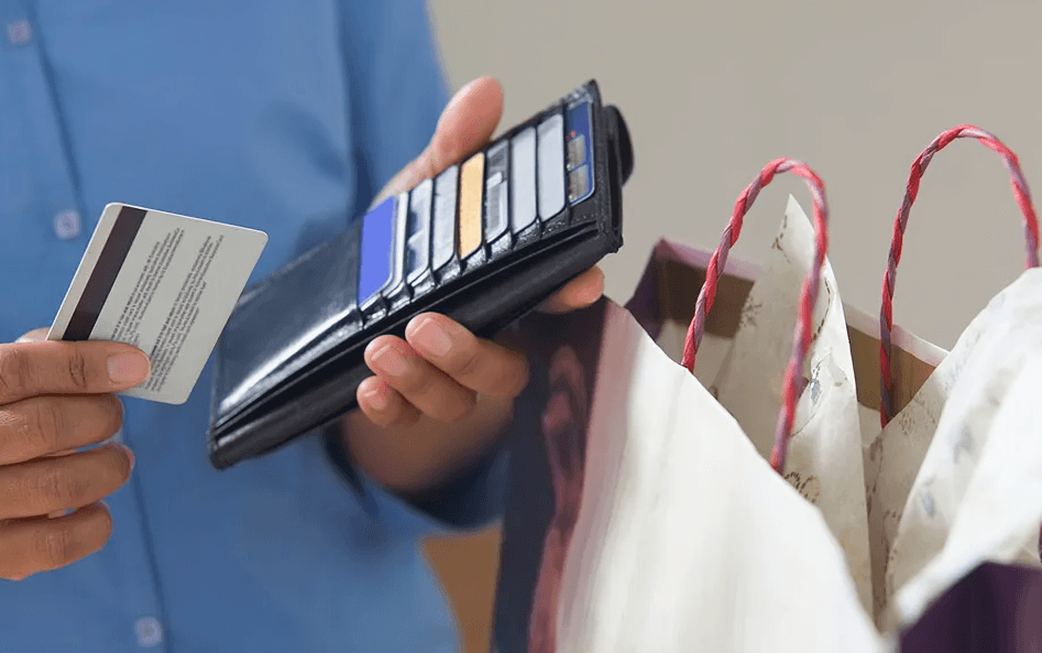 Hand holding credit card, open wallet, and shopping bags.