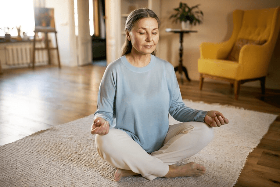 A senior woman meditating on a rug with closed eyes.