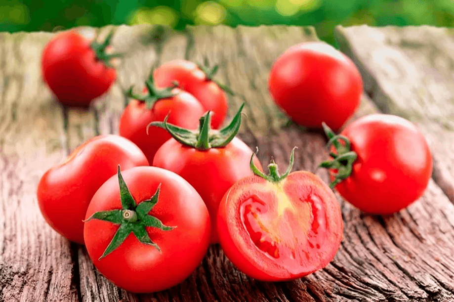 Fresh red tomatoes, one sliced, on wood.