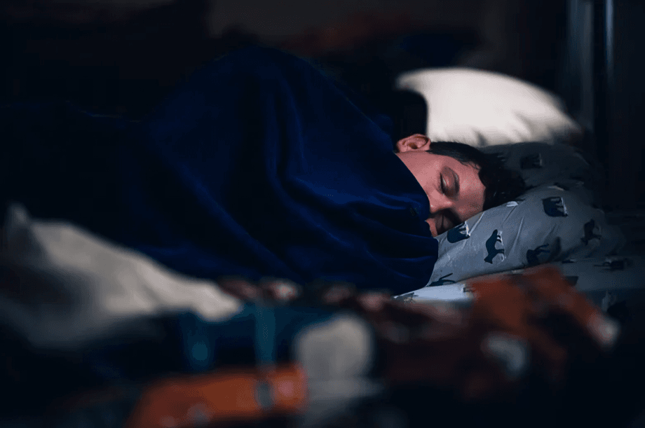 A man sleeping soundly under a blue blanket.