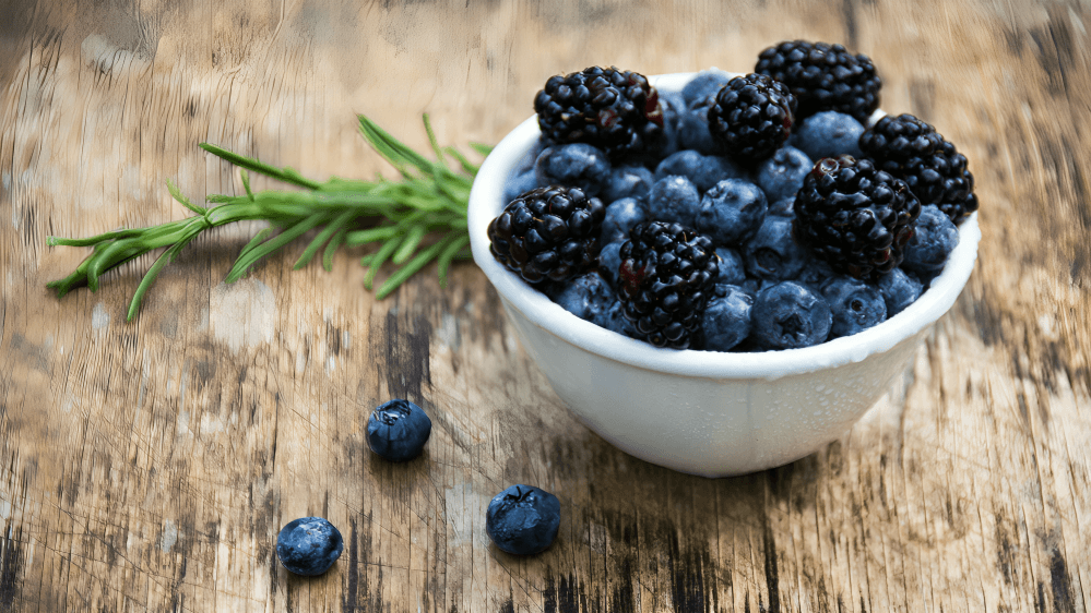 A bowl of blueberries and blackberries with rosemary.
