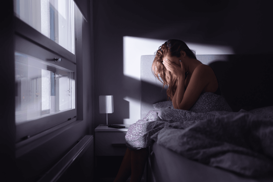 Woman sitting in bed, head in hands, looking distressed.