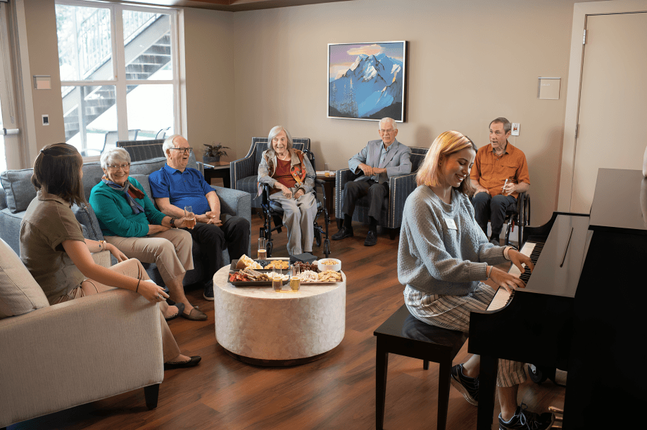 A woman plays piano for smiling seniors in lounge.