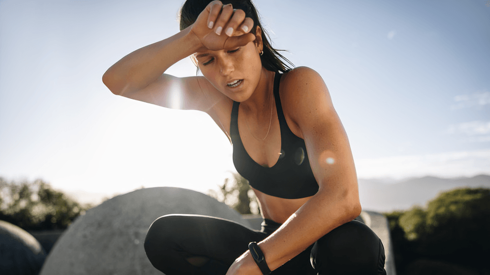 A sweaty woman rests after a workout, hand on forehead.