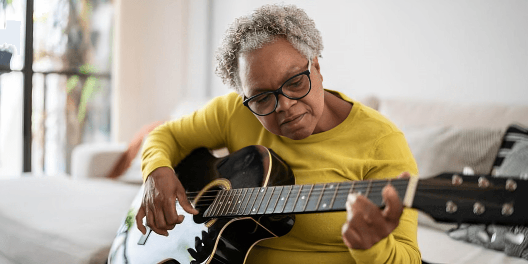 Senior woman with glasses playing an acoustic guitar.